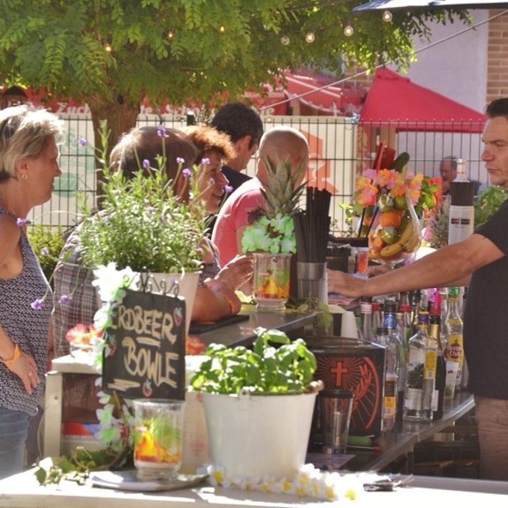 Besucher stehen an einer dekorierten Cocktailbar im Außenbereich des Fests.